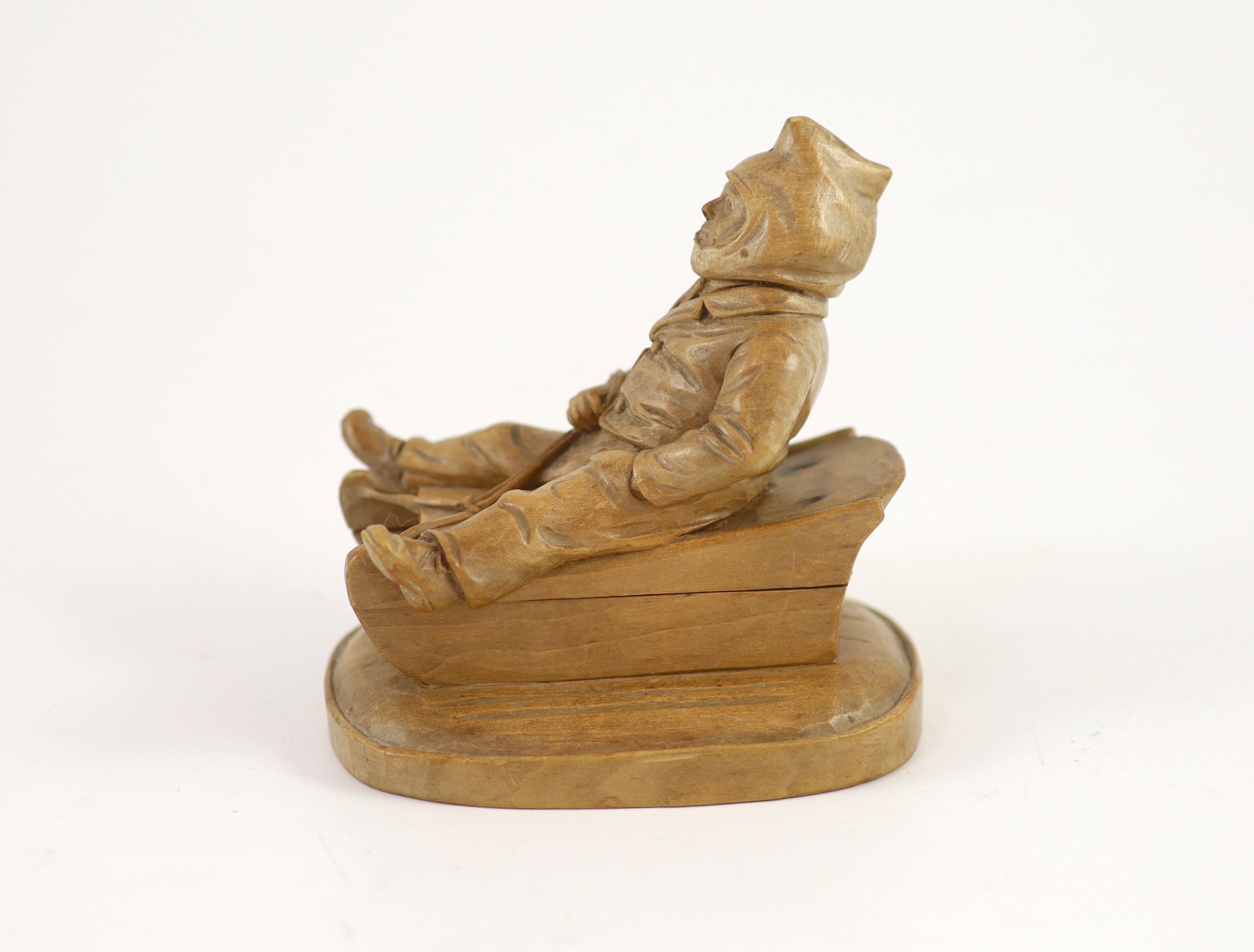 A North European novelty carved beech inkwell in the form of a seated figure sledging, c.1900, 11cm high, 11cm long.